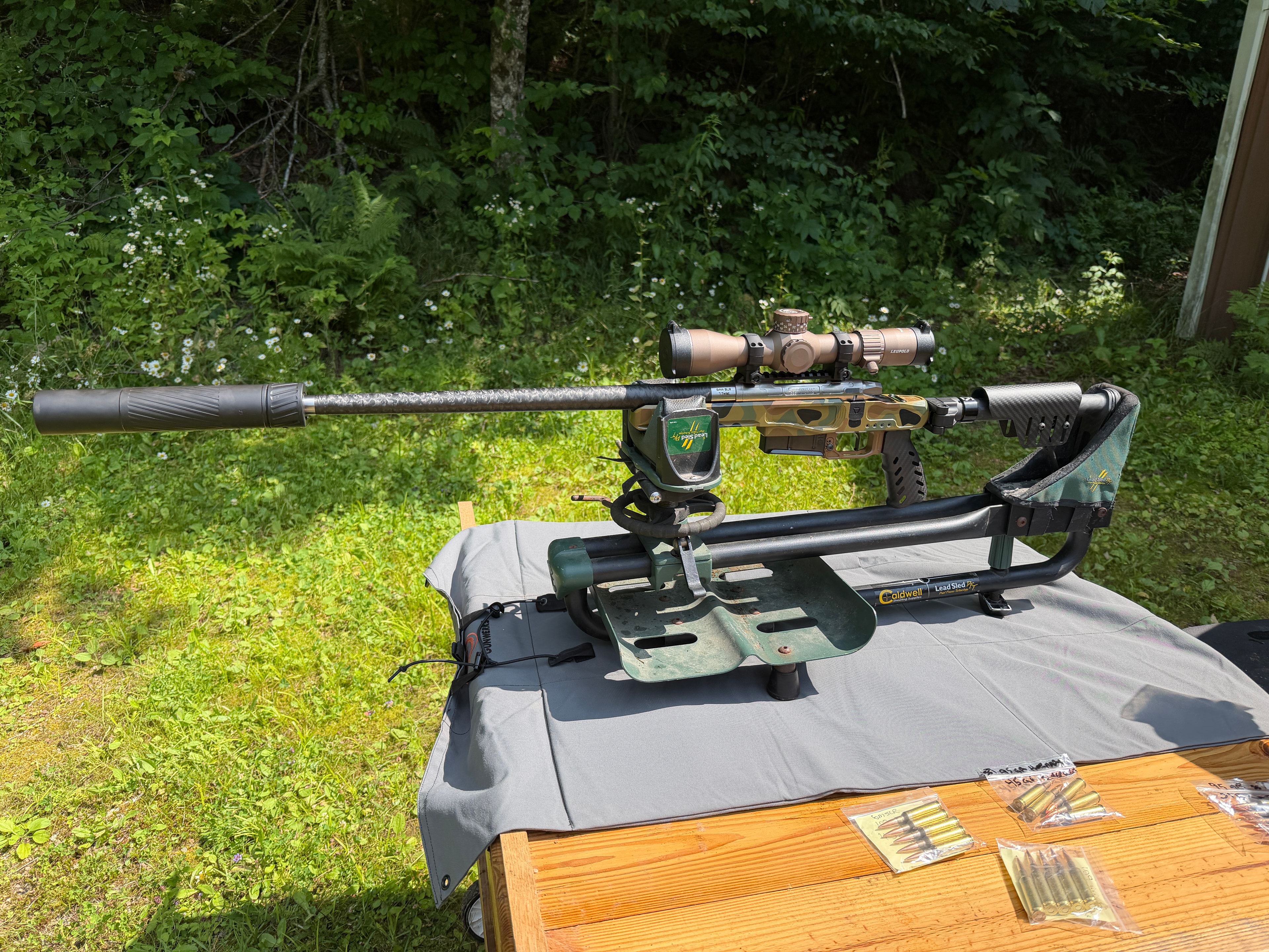 Custom camo precision bolt-action rifle with carbon fiber barrel, suppressor, and Leupold scope resting on a Caldwell Lead Sled shooting rest — custom build by Northwoods Firearms, Crandon, WI