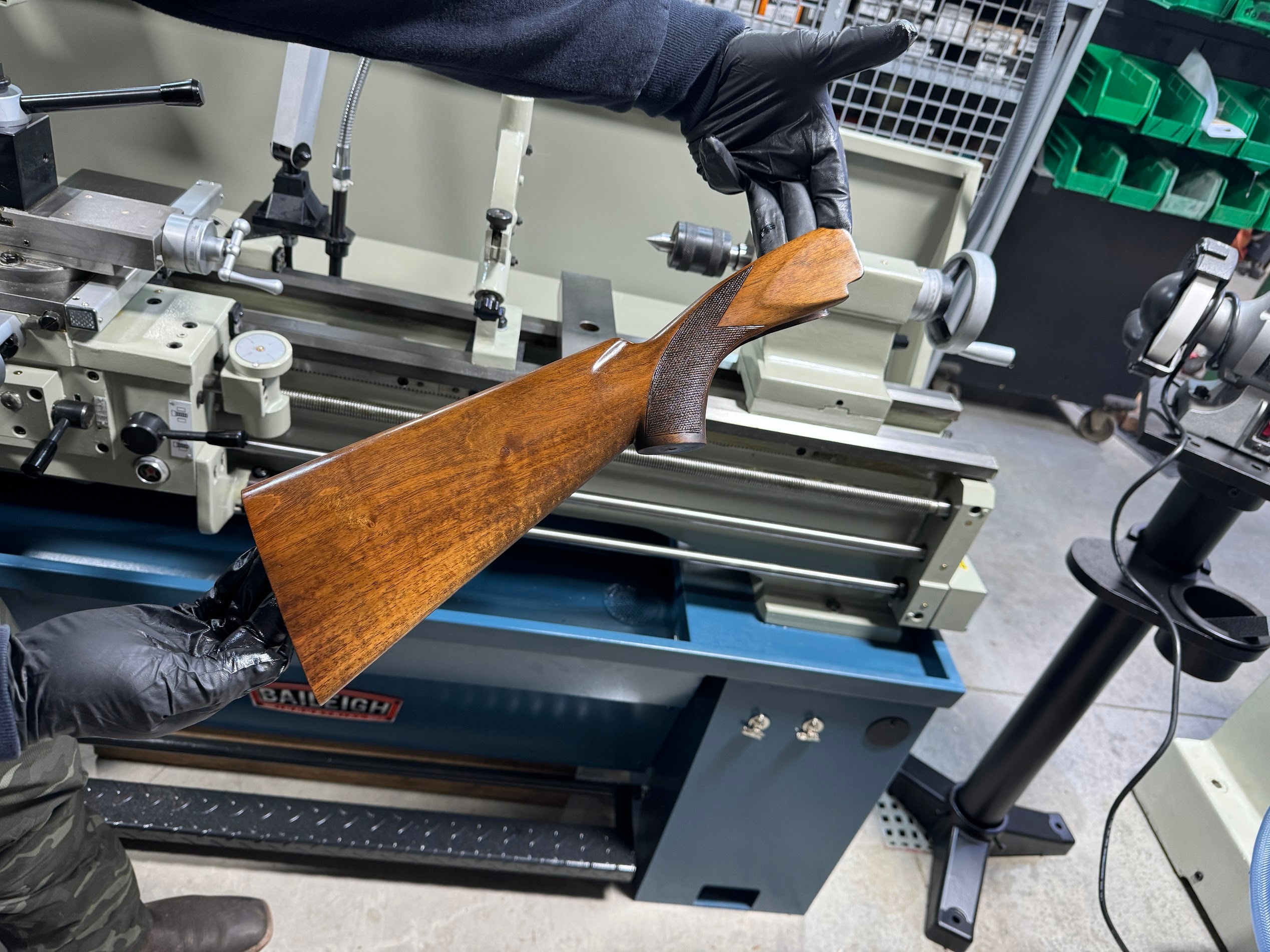 Bobby Connor holding a hand-fitted walnut shotgun stock in the Northwoods Firearms machine shop, Baileigh lathe in background