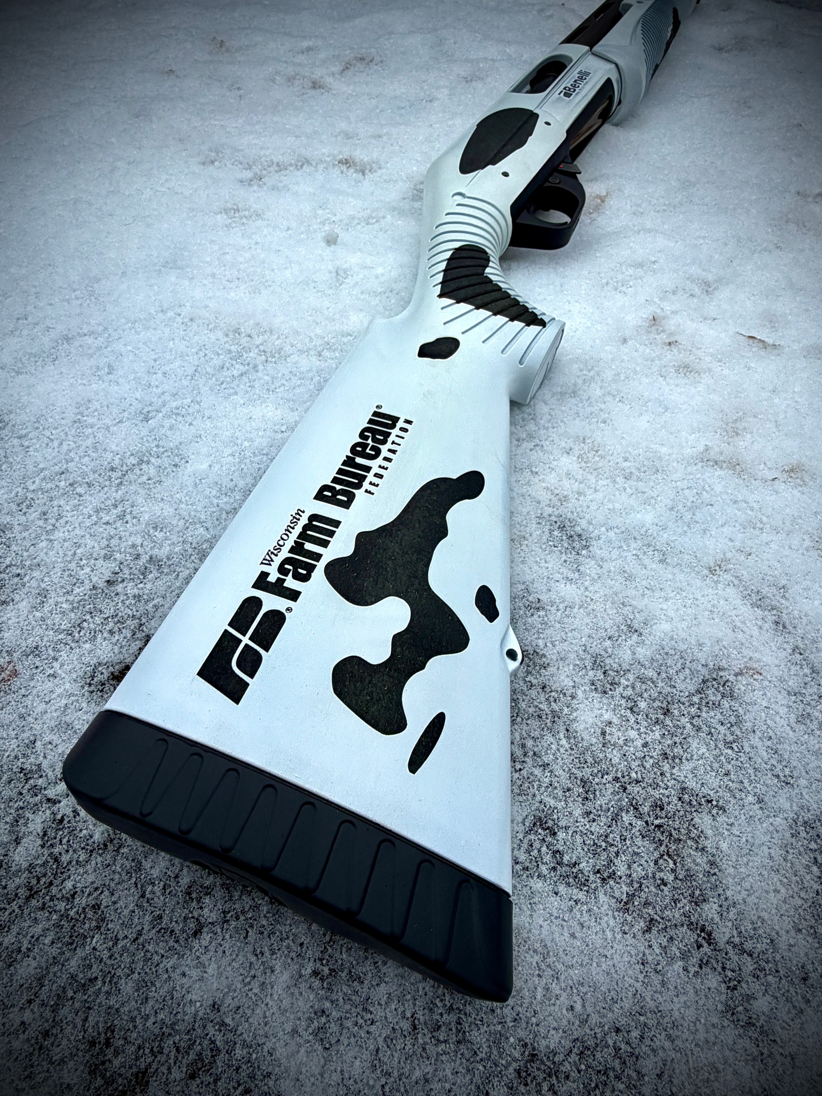 Laser-engraved Benelli Nova pump-action stock with Wisconsin Farm Bureau Federation logo and cow-spot pattern on white and black finish — by Northwoods Firearms