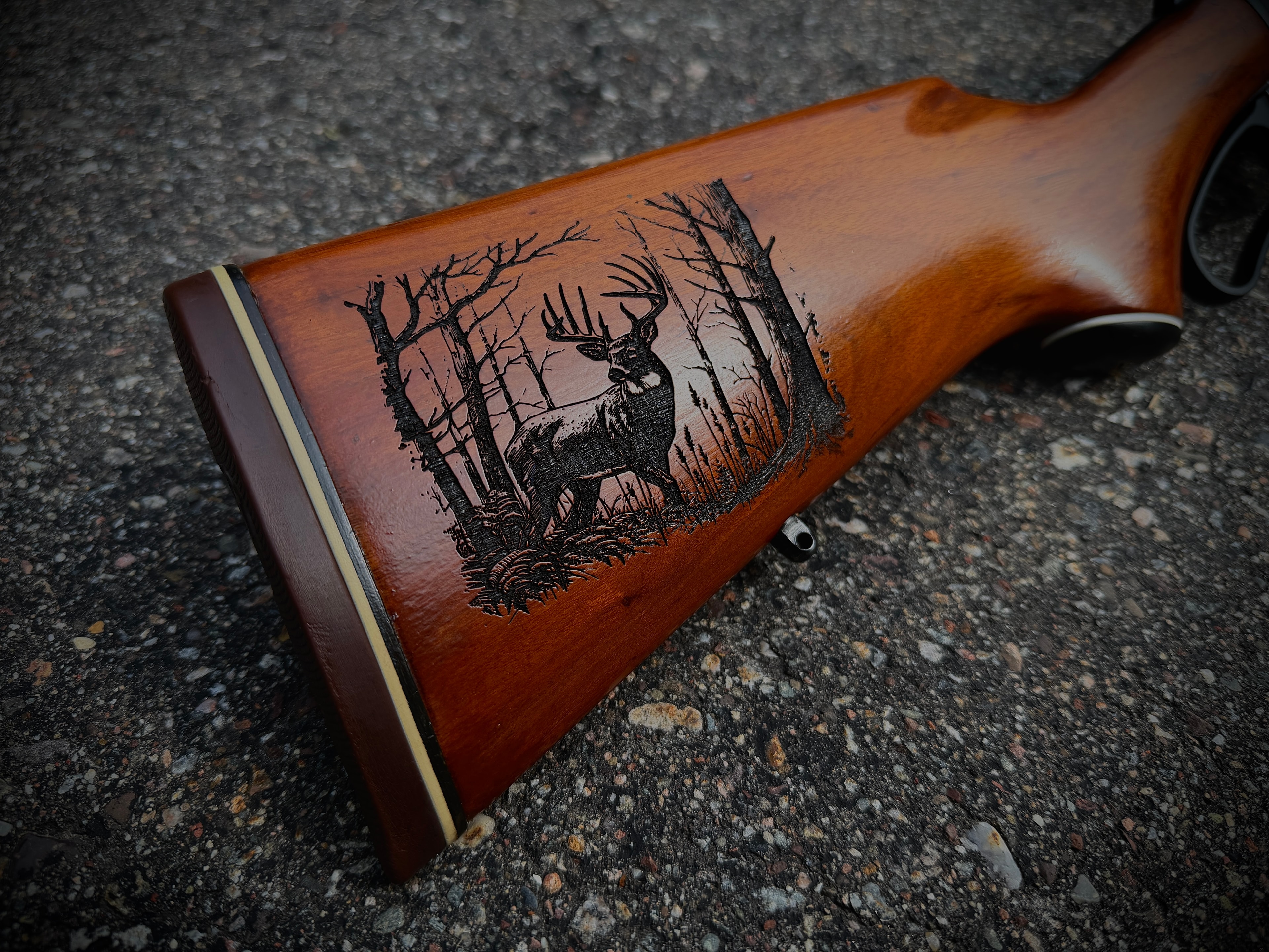 Laser-engraved whitetail deer standing in a winter forest scene on walnut rifle stock by Northwoods Firearms, Crandon, WI