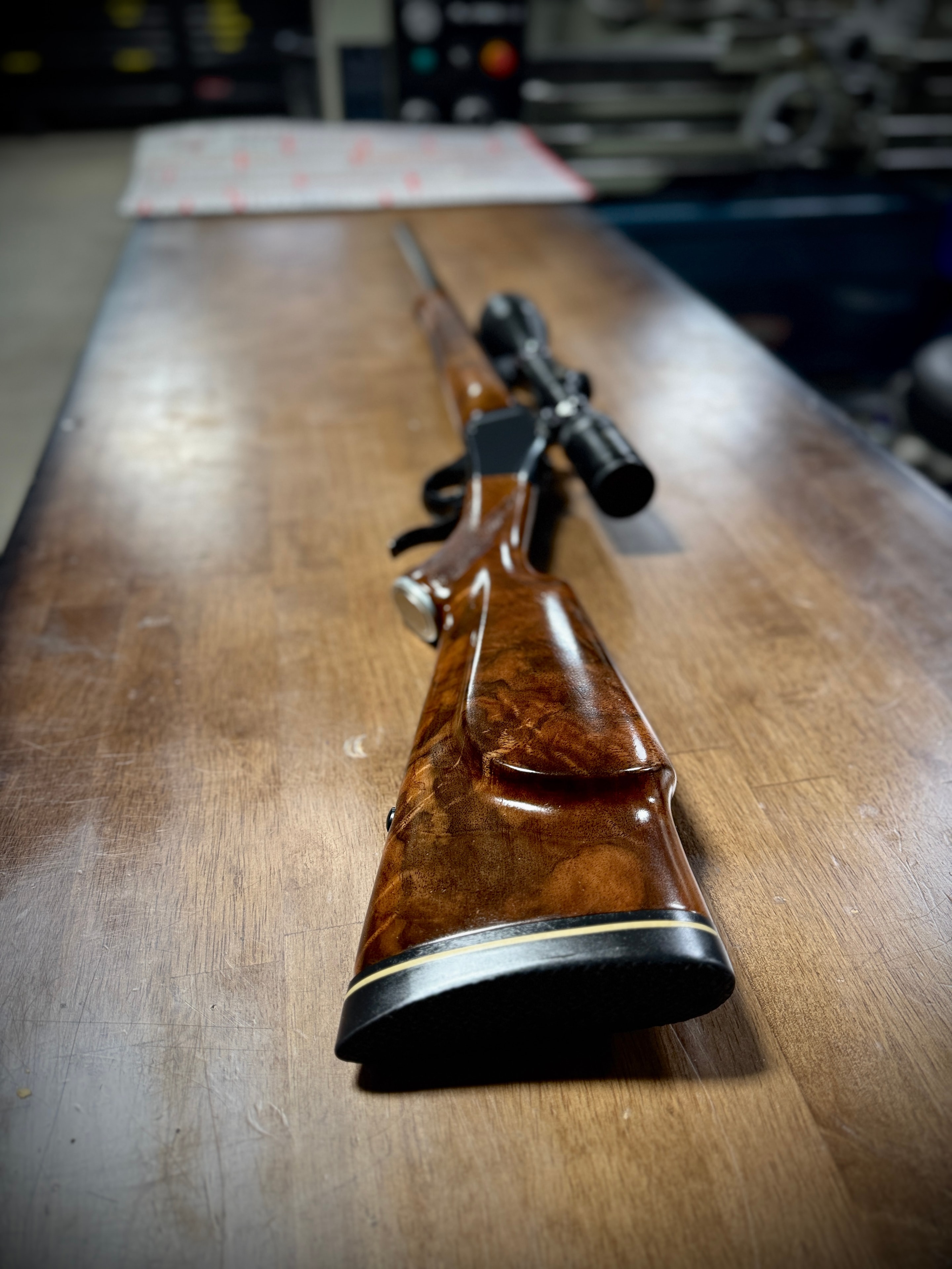 Fully restored bolt-action rifle with custom hand-fitted figured walnut stock, hand checkering, and scope — full profile on workbench at Northwoods Firearms
