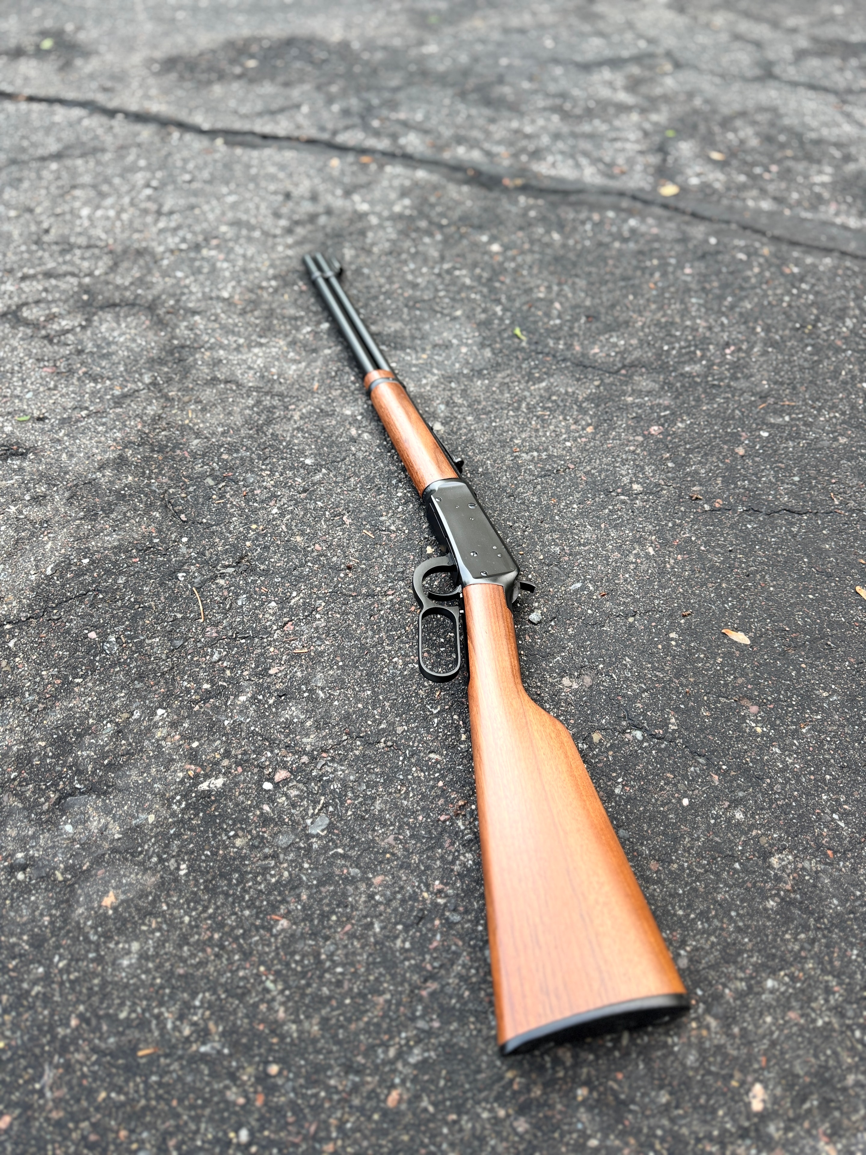 Restored lever-action rifle — full-length profile on pavement showing reblued barrel and action with refinished walnut stock — by Northwoods Firearms, Crandon, WI