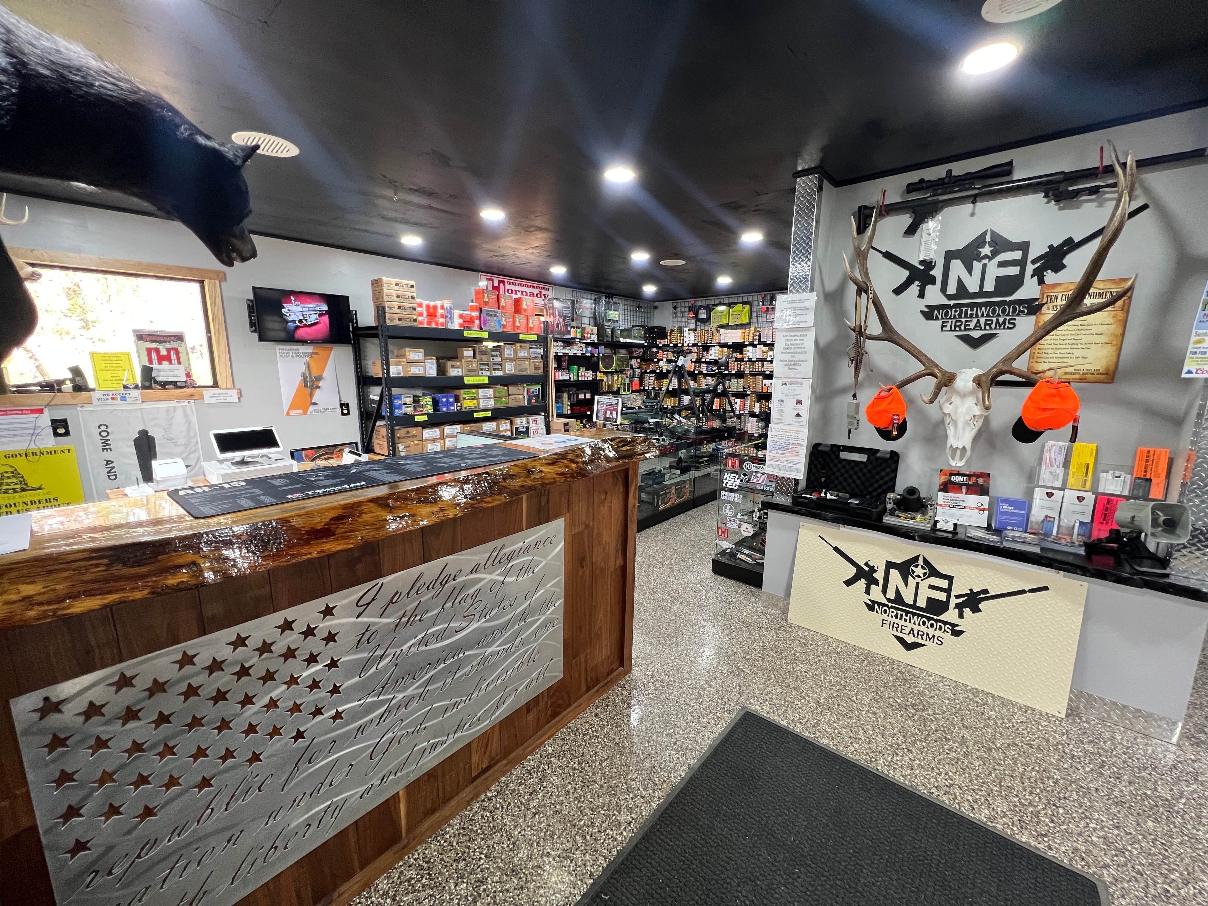 Northwoods Firearms front counter — custom Pledge of Allegiance laser-cut steel panel, NF logo display, bear and elk mounts